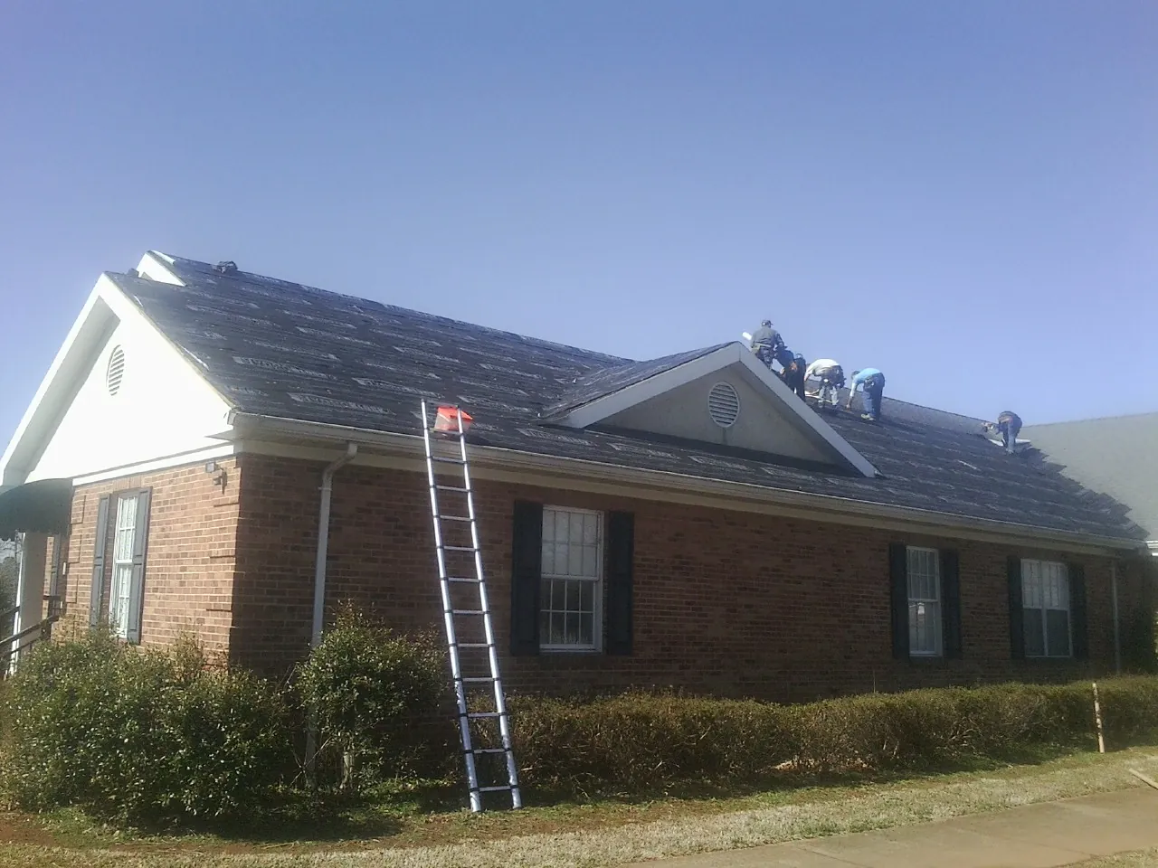 Crew tearing shingles off a brick ranch roof with a ladder set — Emergency Roof Repair work by our crew in Callahan