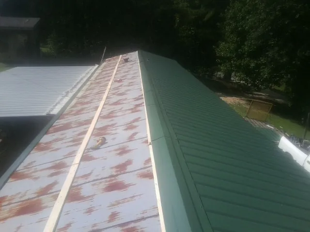 Old rusted panels beside newly installed green metal roofing — Wind Damage Roof Repair by Roofing Brothers in Callahan